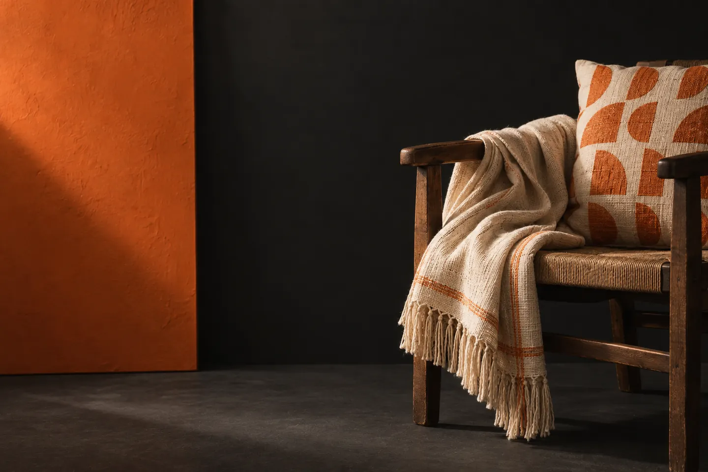 Wooden chair with a cream throw and orange-patterned cushion against a charcoal wall